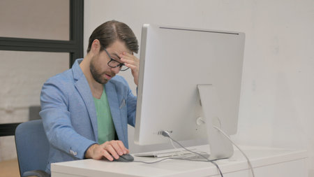 Young Man having Headache while Working on Desktopの写真素材