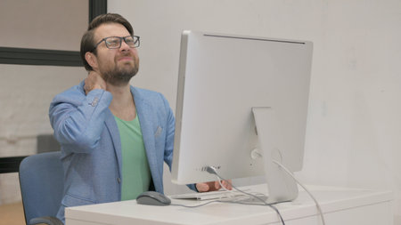 Young Man having Neck Pain while Working on Desktop