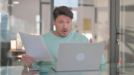 Man Shocked by Loss while Working on Documents and Laptopの写真素材