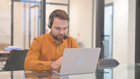 Young Man with Headset Talking with Customer via Laptop