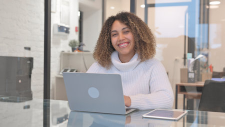 African Woman Smiling at Camera while Working on Laptop in Officeの写真素材