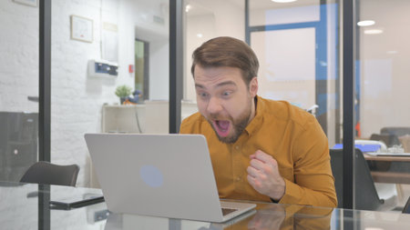 Excited Businessman Celebrating Success on Laptop in Officeの写真素材