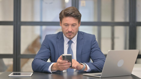 Middle Aged Businessman Browsing Internet on Phoneの写真素材