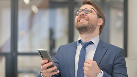 Portrait of Middle Aged Businessman Celebrating Success on Phoneの写真素材