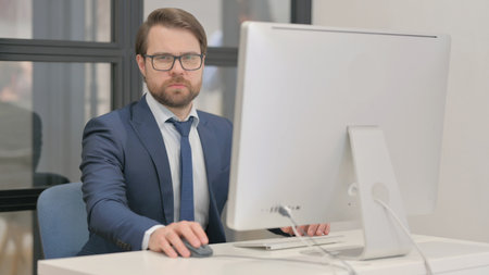 Young Businessman Looking at Camera while Working on Computerの写真素材