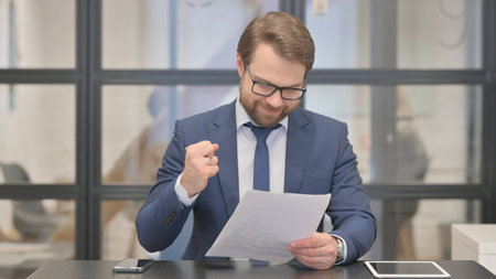 Young Businessman Celebrating while Reading Documentsの写真素材