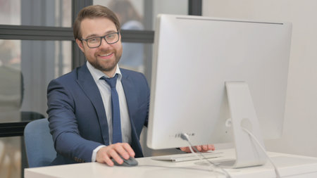 Young Businessman Smiling at Camera while Working on Computerの写真素材