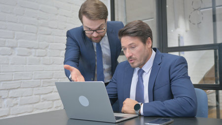 Angry Standing Businessman in Argument with Partner at Work, Using Laptopの写真素材