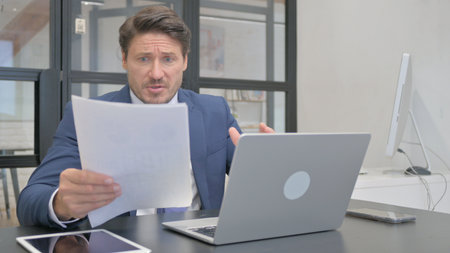 Mature Adult Businessman Shocked while Working on Documents and Laptop