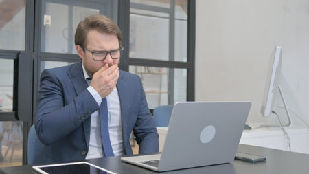 Sick Young Businessman Working in Office and Coughingの写真素材