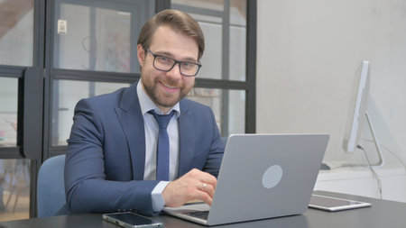 Young Businessman Smiling at Camera while Working on Laptopの写真素材