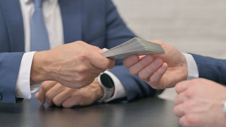 Close-up of two businessmen exchanging money at table in office.の写真素材