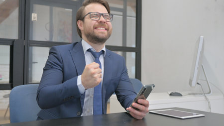 Young Businessman Cheering Online Results on Smartphoneの写真素材