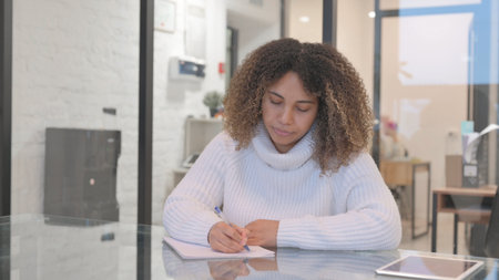 African Woman Writing on Paper in Office