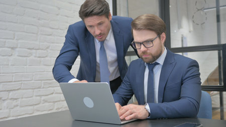 Standing Businessman Discussing Work on Laptop with Teammateの写真素材