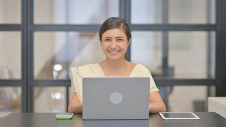 Young Indian Woman Smiling at Camera while Working on Laptopの写真素材