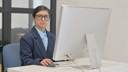 Young Indian Businesswoman Looking at Camera while Working on Desktopの写真素材