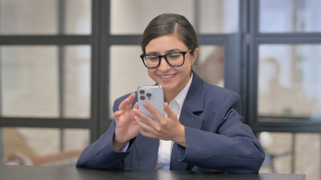 Mixed Race Businesswoman Celebrating Win on Phoneの写真素材