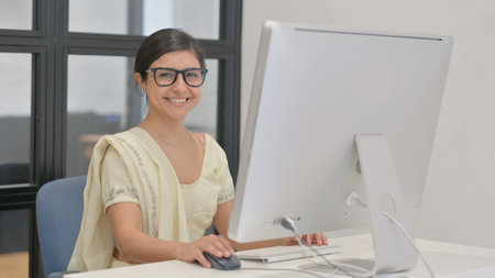 Young Indian Woman Smiling at Camera while Working on Desktop