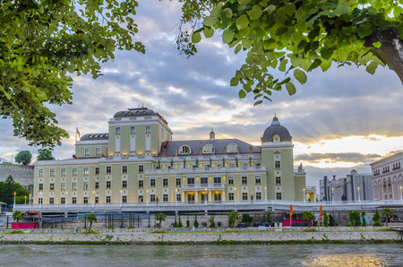 Beautiful colorful sunrise view of vmro museum through the green tree branches near Vardar rever in Skopje, Macedoniaのeditorial素材