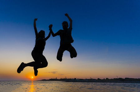 Silhouette Couple Girl and boy jumping on the beach sunset water horizon and clear colorful sky