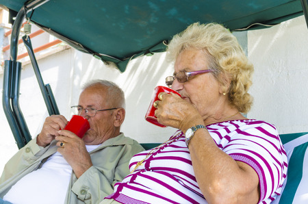 Senior Couple Sitting On A Bench Having Drink Stock Image, focus on femaleの写真素材