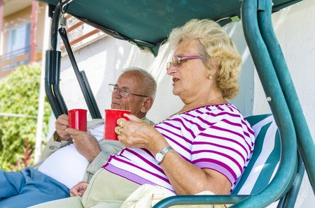 Senior Couple Sitting On A Bench Having Drink Stock Image, focus on maleの写真素材