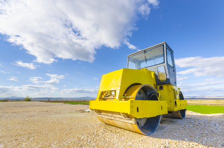 Yellow road-roller on repairing of the road against blue skyの写真素材