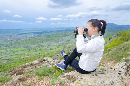 Hiker looking in binoculars enjoying spectacular view on mountain top above the cloudsの写真素材
