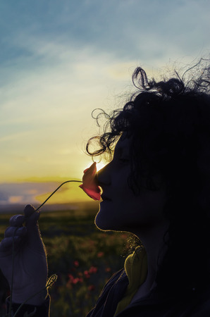 young woman smell poppy flowers on sunset, verticalの写真素材