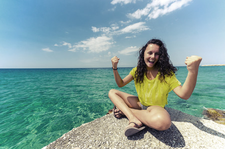 Young teen happy for successful holliday. Girl in yellow contrast shirt sitting at the edge and enjoying nice clean water and sky horizon.の写真素材