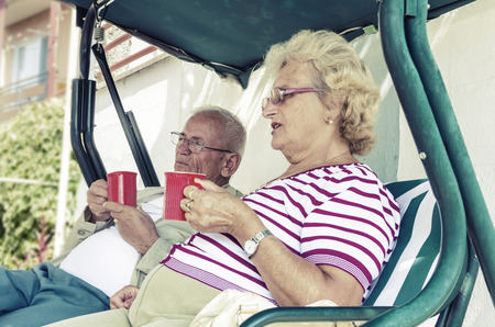Senior Couple Sitting On A Bench Having Drink Stock Image, focus on maleの写真素材