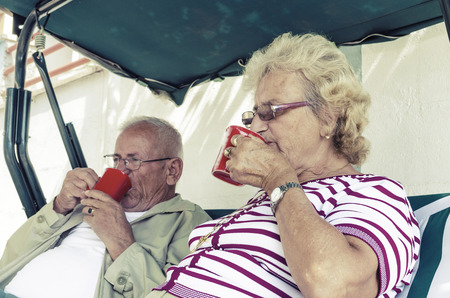 Senior Couple Sitting On A Bench Having Drink Stock Image, focus on femaleの写真素材
