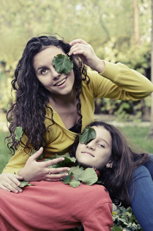 two beautiful teenager having fun playing in the garden with green leafs on their eyesの写真素材
