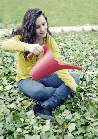 beautiful teenager yellow shirt girl water pouring small tree with red bucketの写真素材