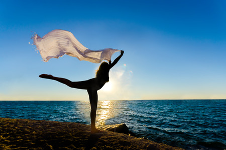 Silhouette of the happy woman with fiber dancing and jumping at the sunset beach sea horizonの写真素材