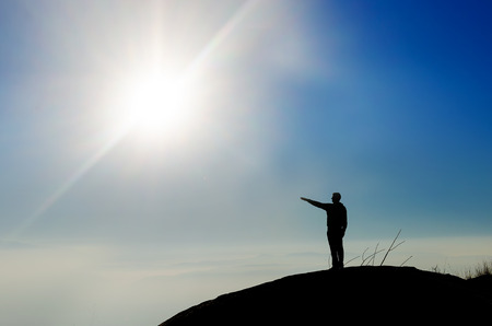Silhouette of a champion on mountain top pointing toward sun. の写真素材
