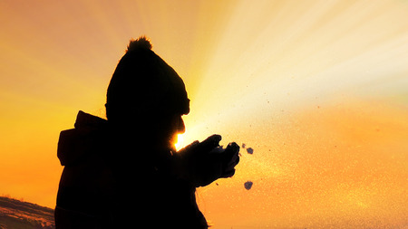 Young female silhouette blowing snow on sunset close upの写真素材