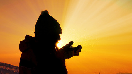 Young female silhouette blowing snow on sunset close upの写真素材