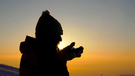 Young female silhouette blowing snow on sunset close upの写真素材