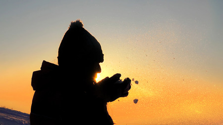 Young female silhouette blowing snow on sunset close upの写真素材