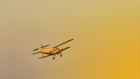 A white crop duster from below fly against the susnetの写真素材