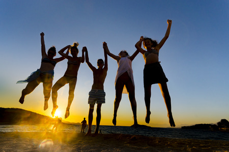 Happy funny people jumping in the sunset on the beachの写真素材