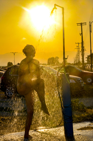 Silhouette of young woman taking a shower outdoors at sunsetの写真素材