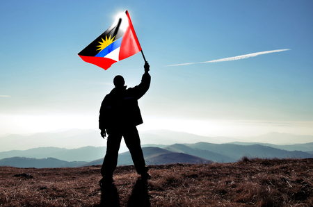 Successful silhouette man winner waving Antigua and Barbuda flag on top of the mountain peakの写真素材