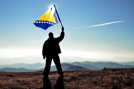 Successful silhouette man winner waving Bosnia And Herzegovinaflag on top of the mountain peakの写真素材