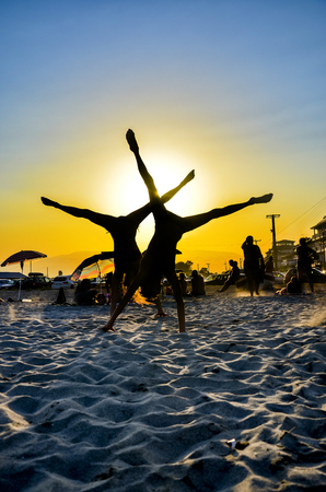 Young couple makes Handstand at the beach with legs wide open at sunset, verticalの写真素材