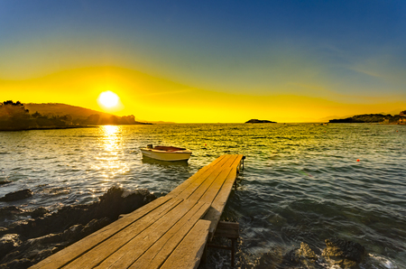 Pier leading out onto the sea sunrise with small boat, long way outの写真素材