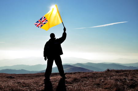 Successful silhouette man winner waving Niue flag on top of the mountain peakの写真素材