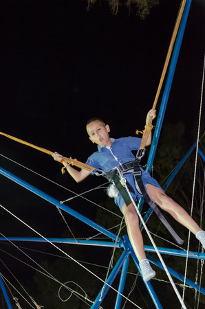 Little boy bungee jumping at trampoline at nightの写真素材